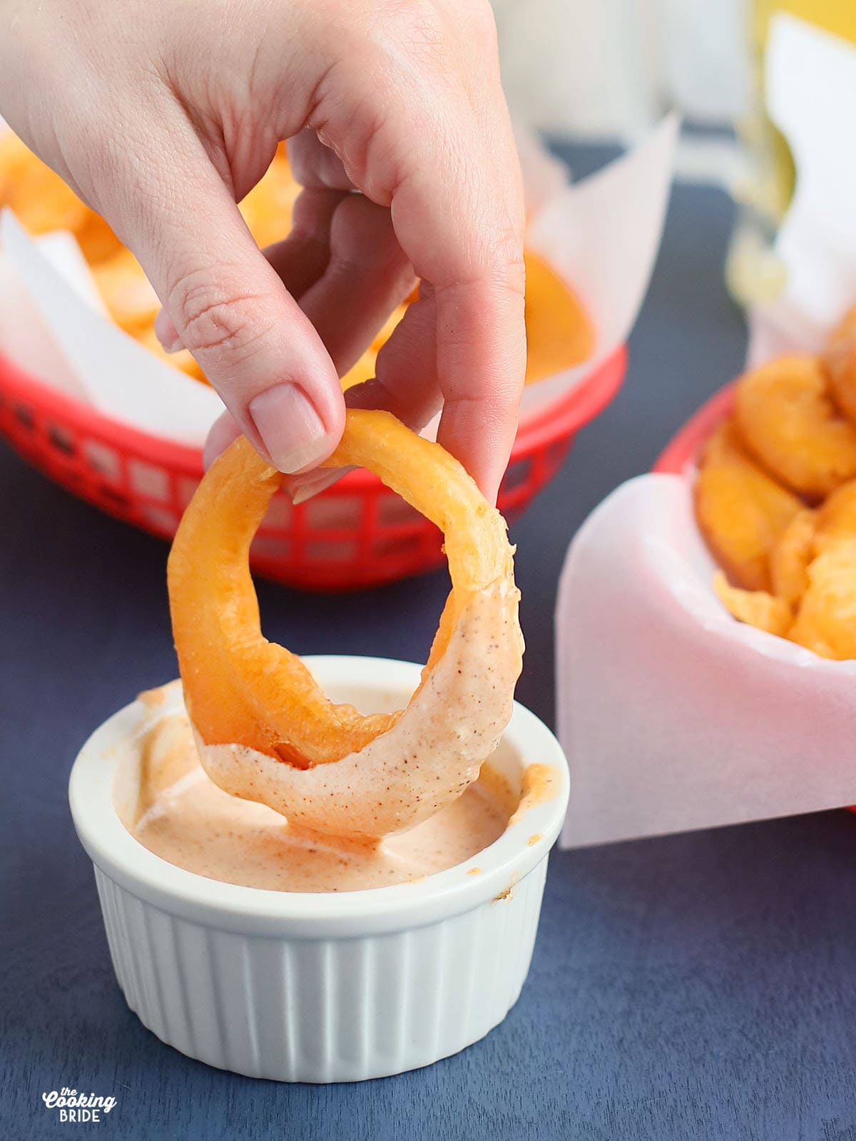 hand dipping a beer battered onion ring to a small bowl of dipping sauce