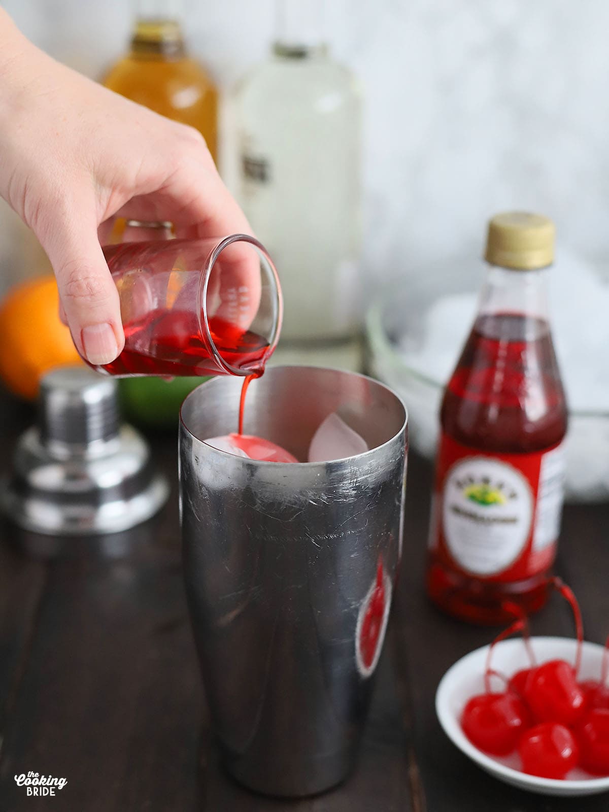 hand pouring grenadine into a cocktail shaker
