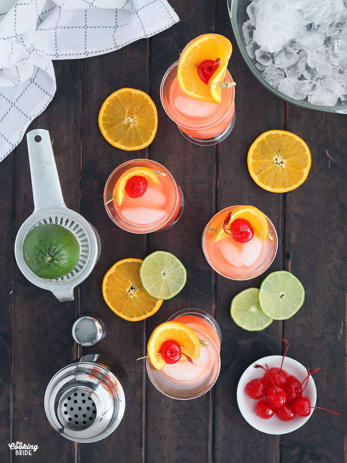 overhead shot of four hurricane cocktails garnished with a cherry and orange slices, sliced limes, oranges and a bowl of ice to the side