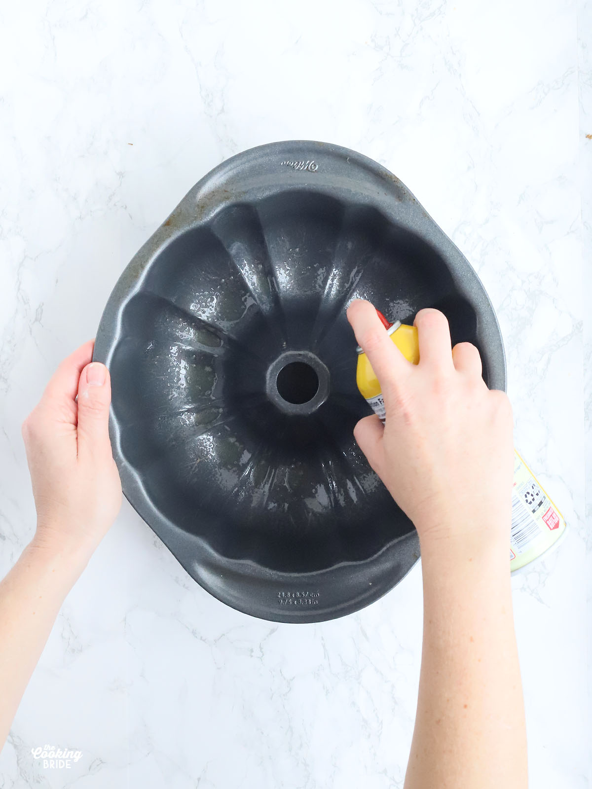 hands spraying a Bundt cake pan with cooking spray