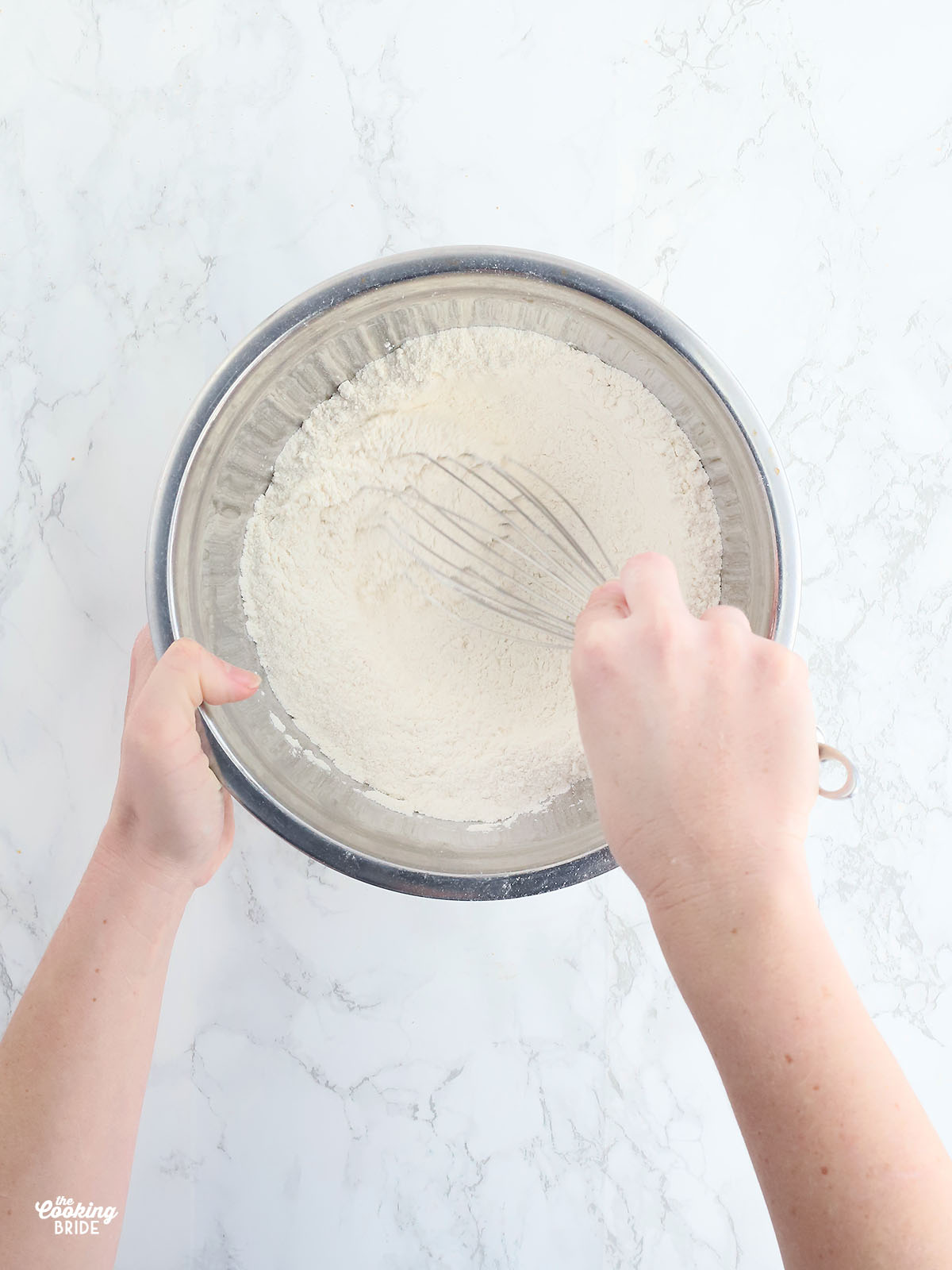 hand whisking dry corn bread ingredients together in a stainless steel mixing bowl