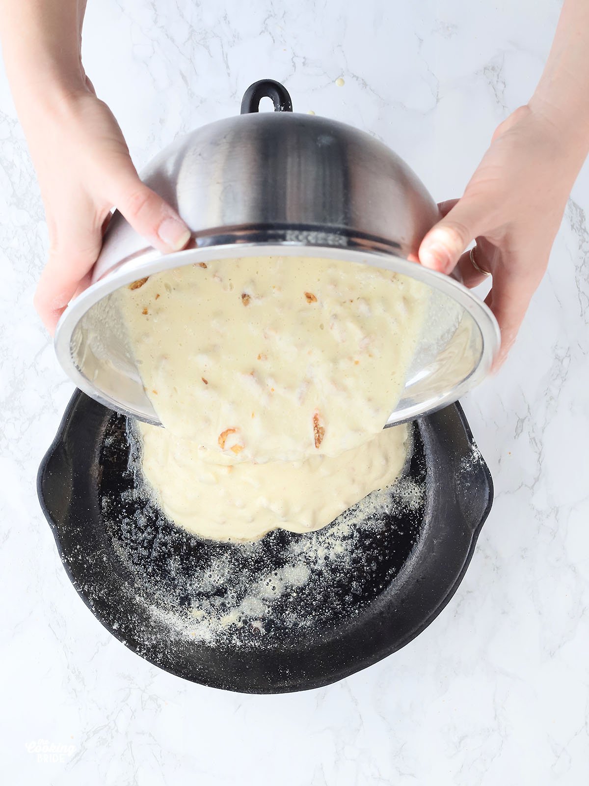 hands pouring cracklin' corn bread batter into a cast iron skillet