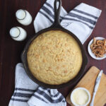 overhead shot of cracklin' corn bread in a cast iron skillet with butter, milk and a dish or cracklings to the side