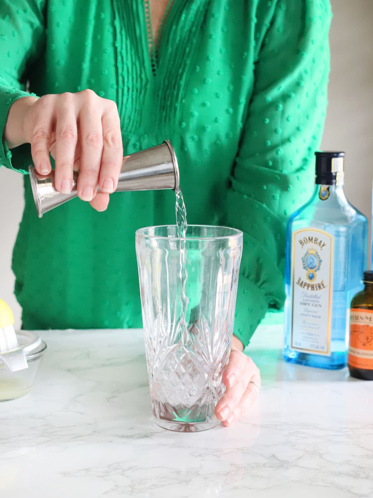 pouring gin from a metal jigger into a glass tumbler