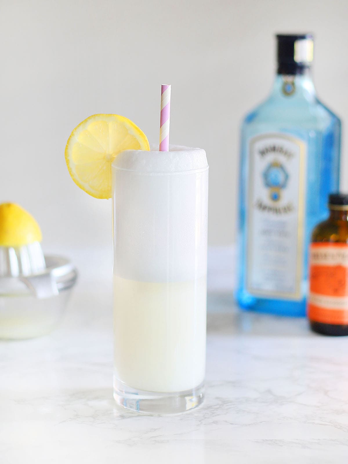 Ramos gin fizz garnished with a lemon slice and a straw on a marble table top
