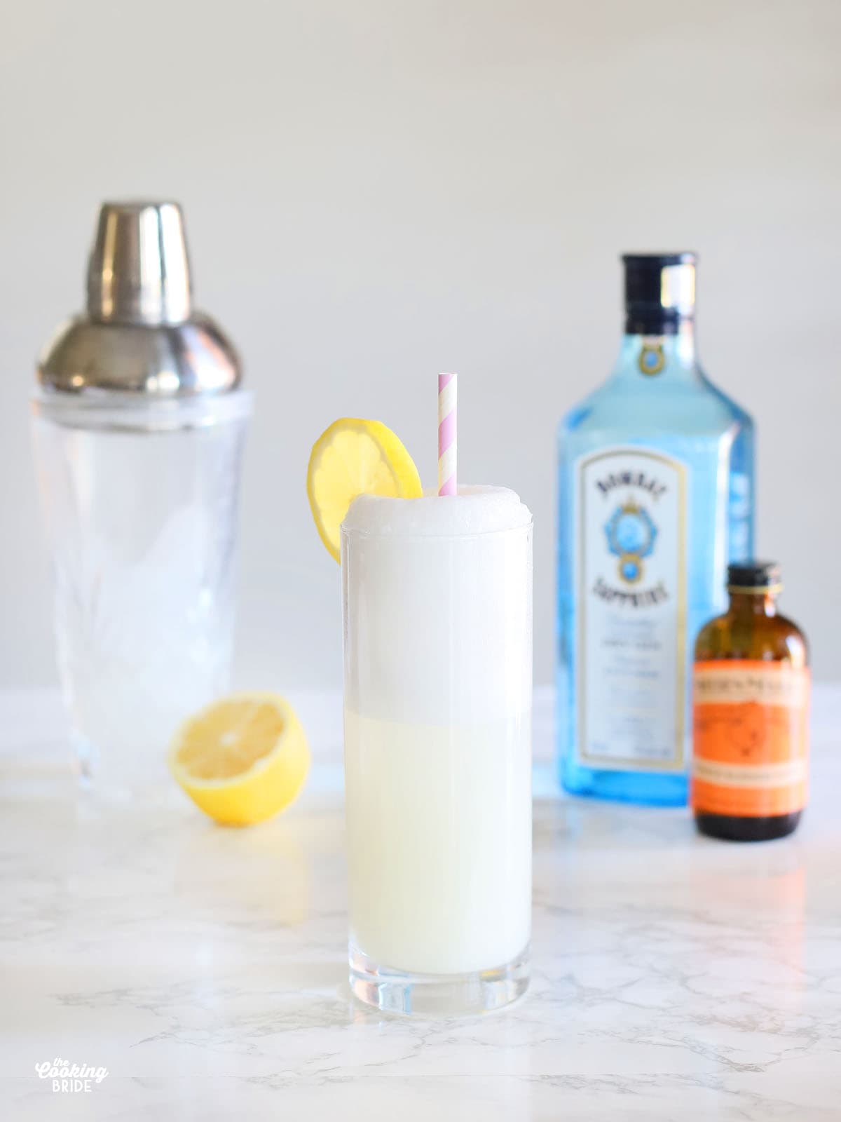 Ramos gin fizz garnished with a lemon slice and a straw on a marble table top