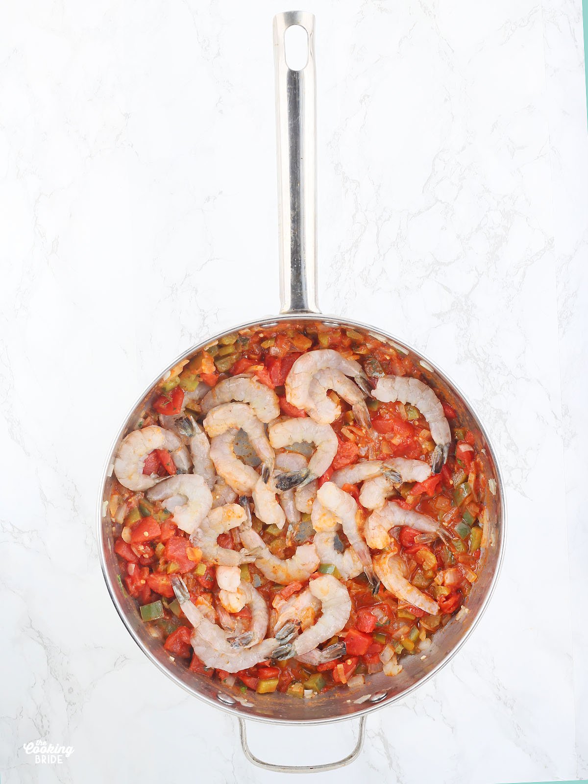 adding the raw shrimp to the pan with tomatoes and vegetables