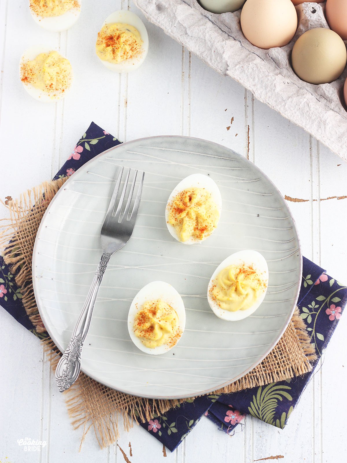three deviled eggs and a fork on a gray plate with a dozen eggs to the side