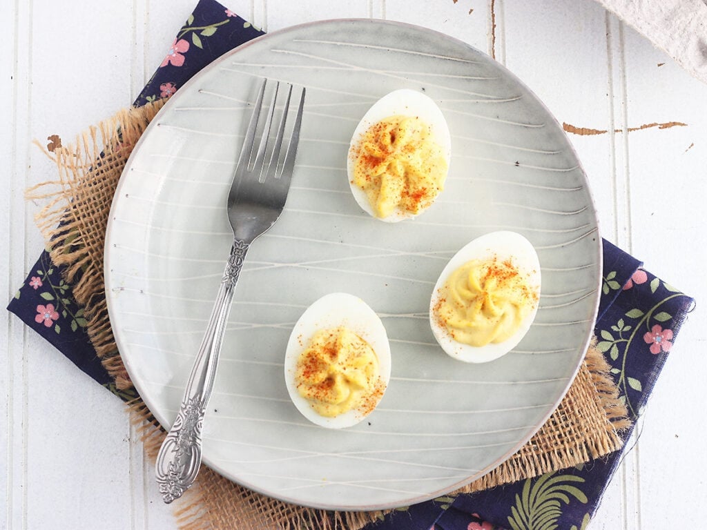 Three deviled eggs and a fork on a gray plate.