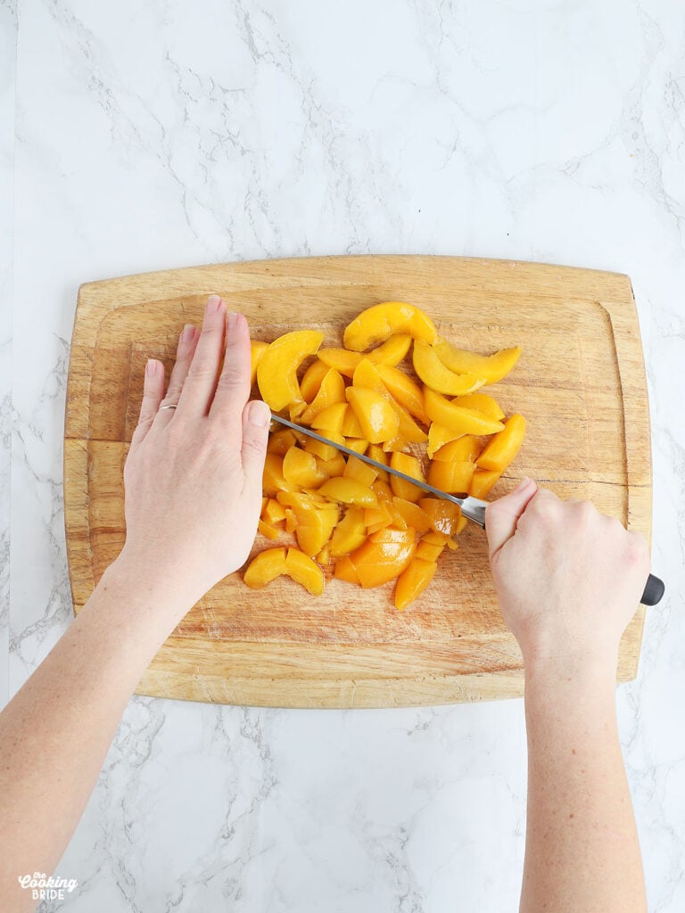 hands chopping canned peaches on a wooden cutting board