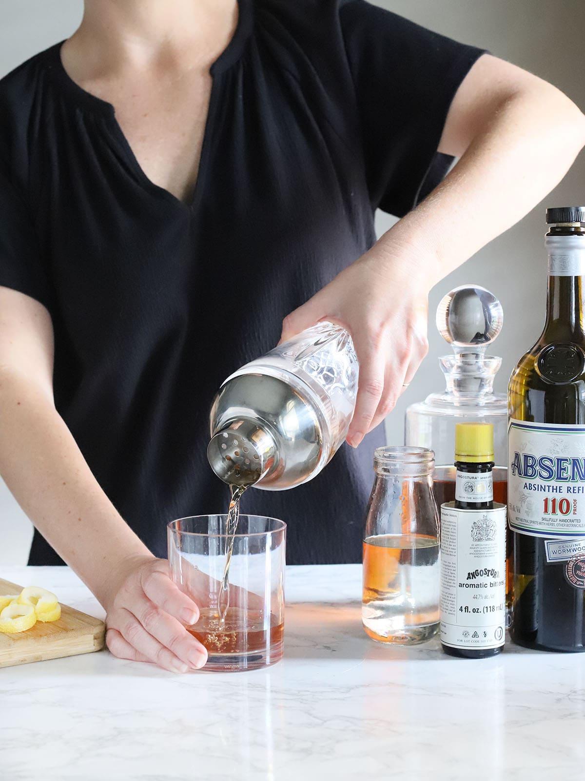 person straining bourbon Sazerac ingredients into an old fashioned glass