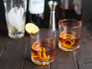 two bourbon Sazeracs with a tumbler and bottles of spirits in the background