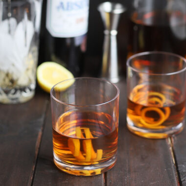 two bourbon Sazeracs with a tumbler and bottles of spirits in the background