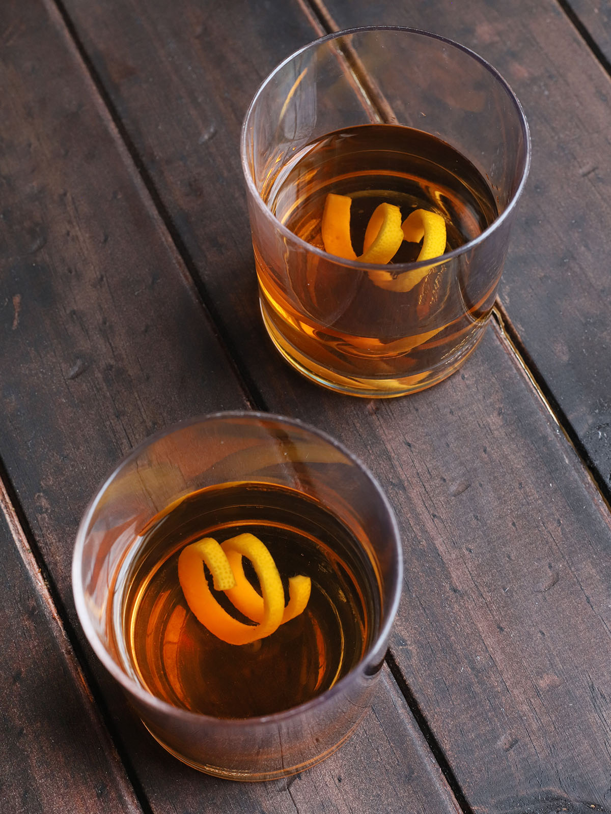 two old fashioned glasses of bourbon sazerac on a dark wooden background