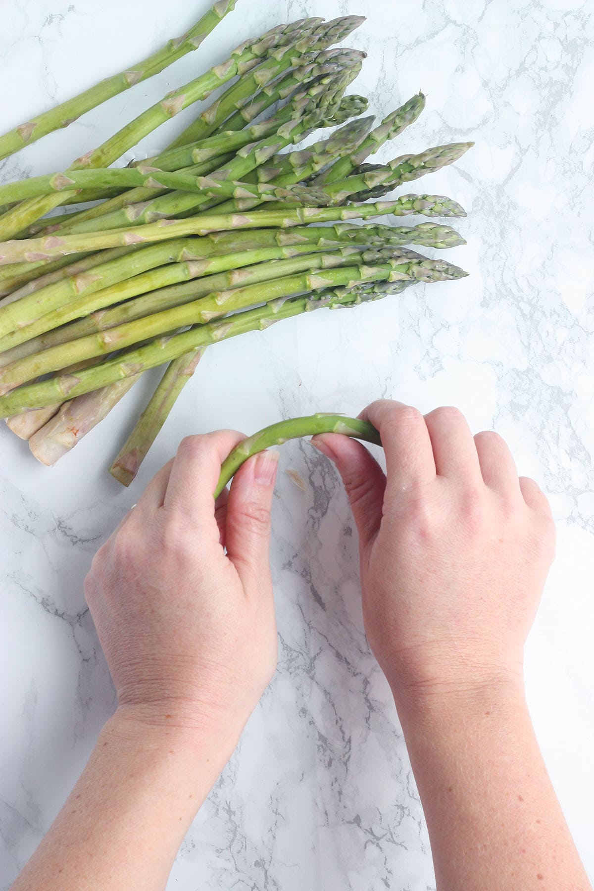 hands bending an asparagus spear to remove the tough, woody end