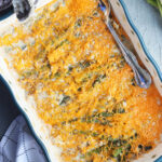 pair of hands placing a baked asparagus casserole onto a grey surface