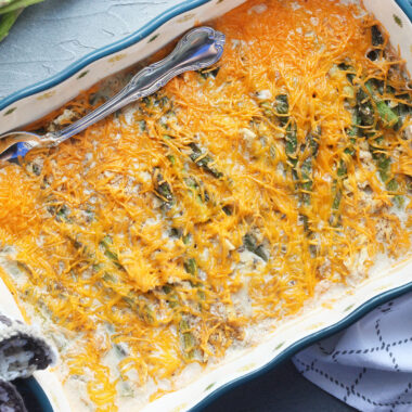 pair of hands placing a baked asparagus casserole onto a grey surface