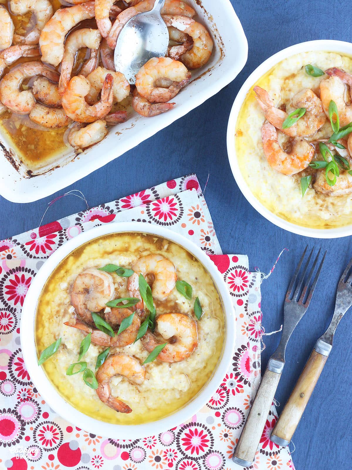 white bowl of barbcue shrimp and grits garnished with sliced green onions on a blue background