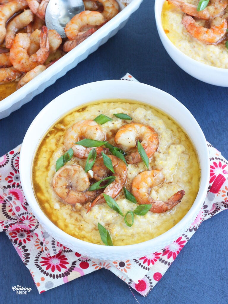 white bowl of barbcue shrimp and grits garnished with sliced green onions on a blue background