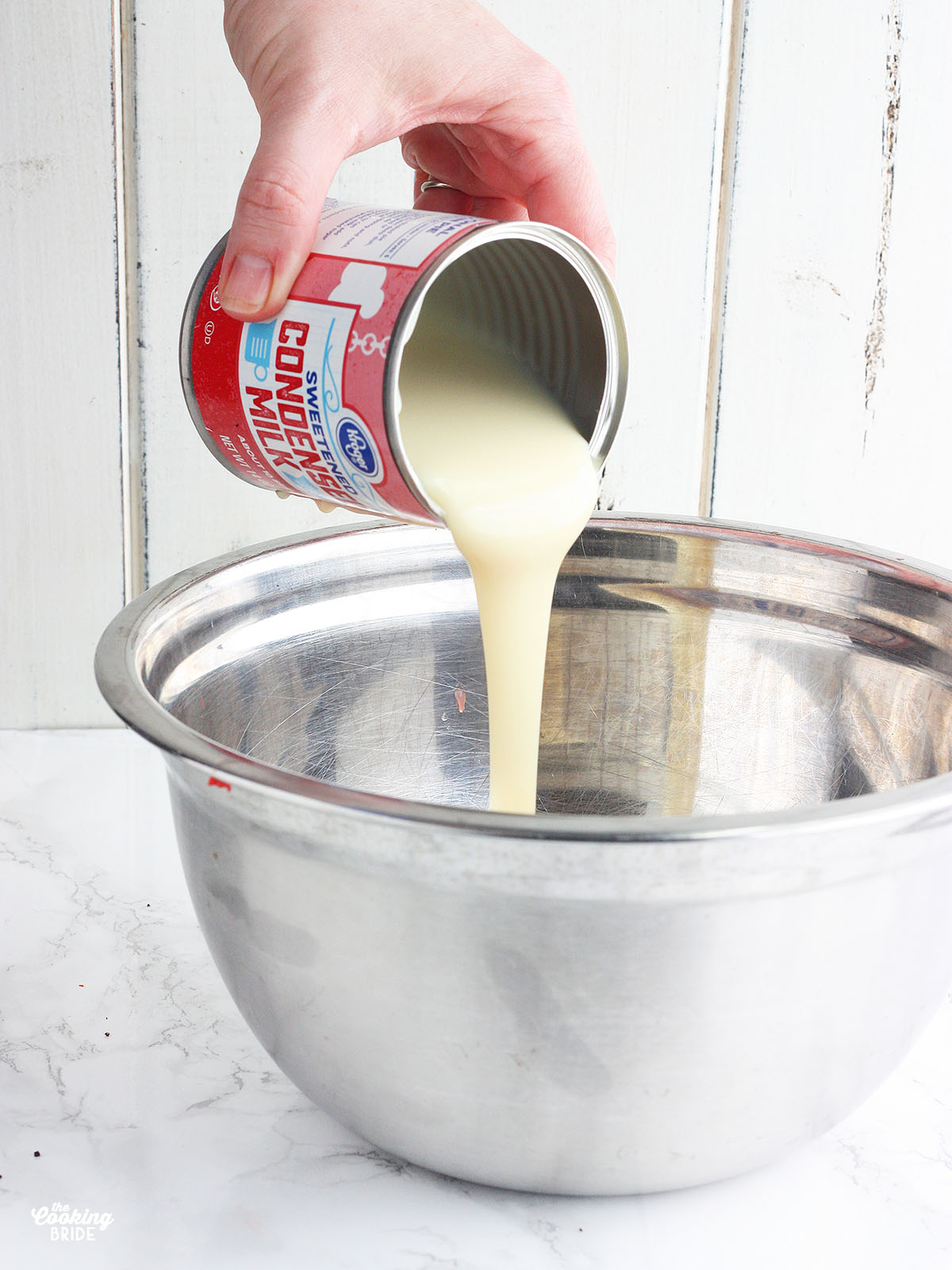 pouring condensed milk into a metal mixing bowl