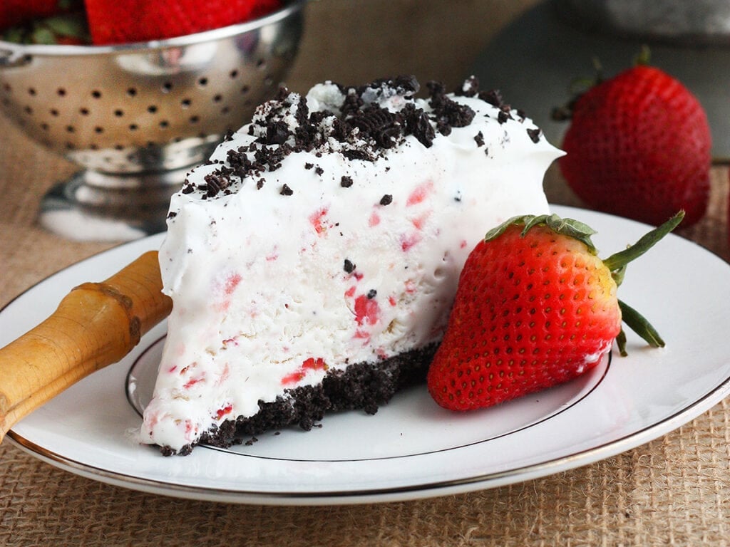 slice of strawberry ice cream cake on a white plate with cake in the background