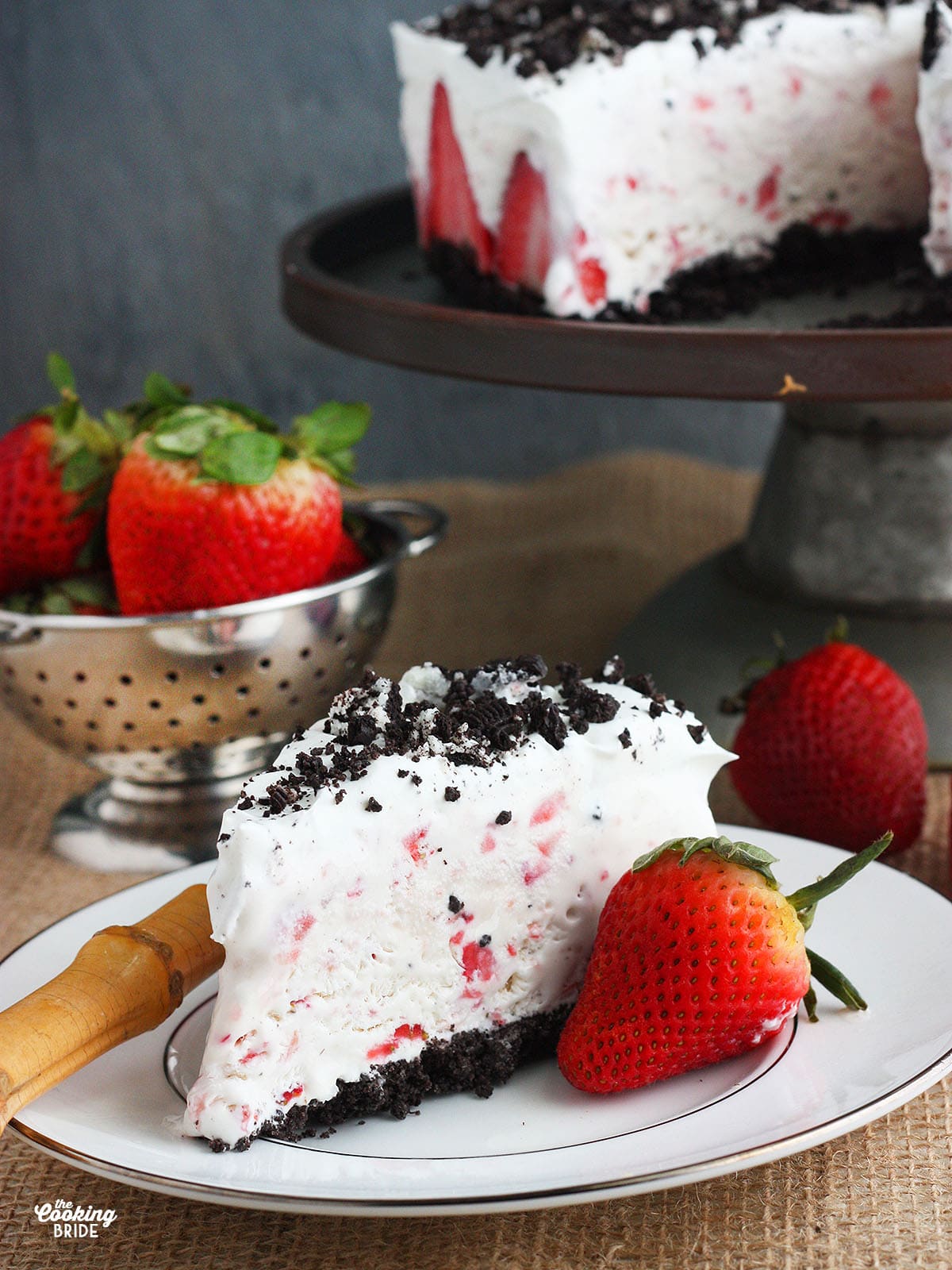 slice of strawberry ice cream cake on a white plate with cake in the background