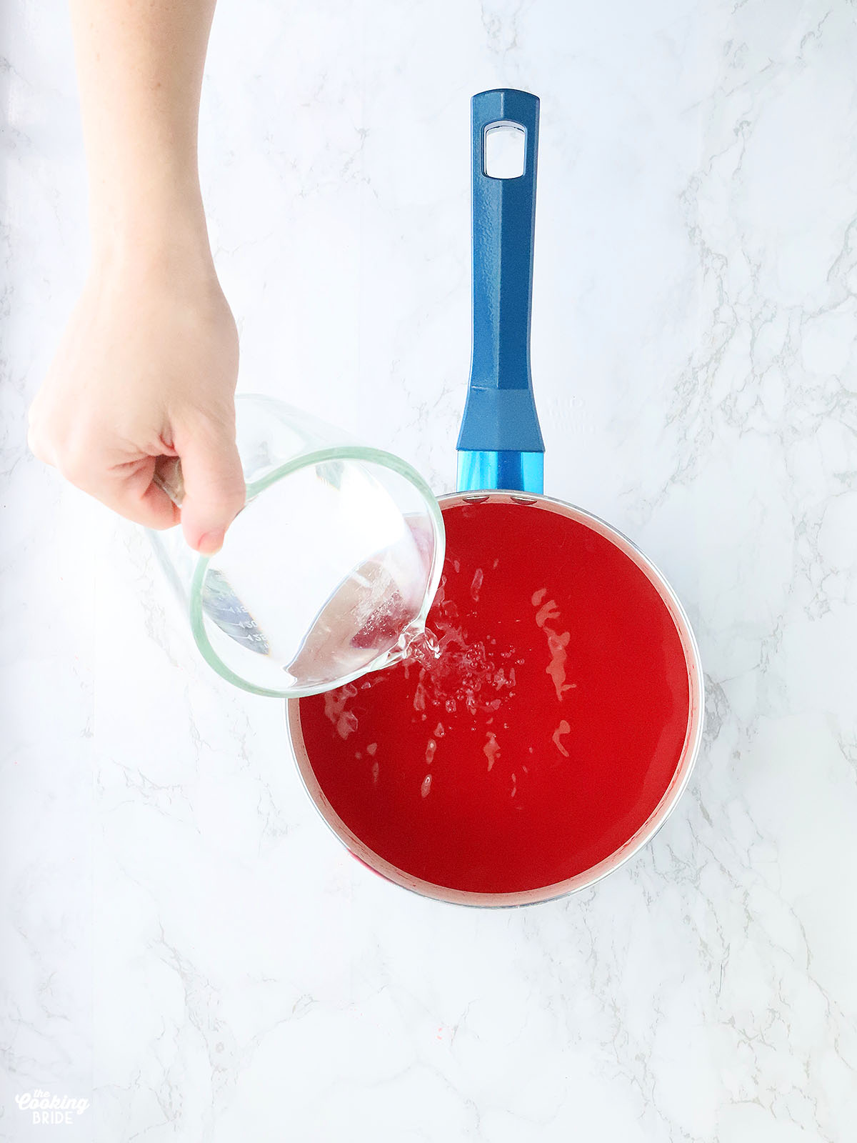 pouring cold water into dissolved strawberry gelatin