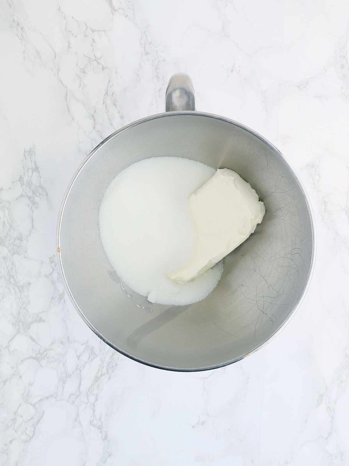 sugar and a block of cream cheese in a metal mixing bowl