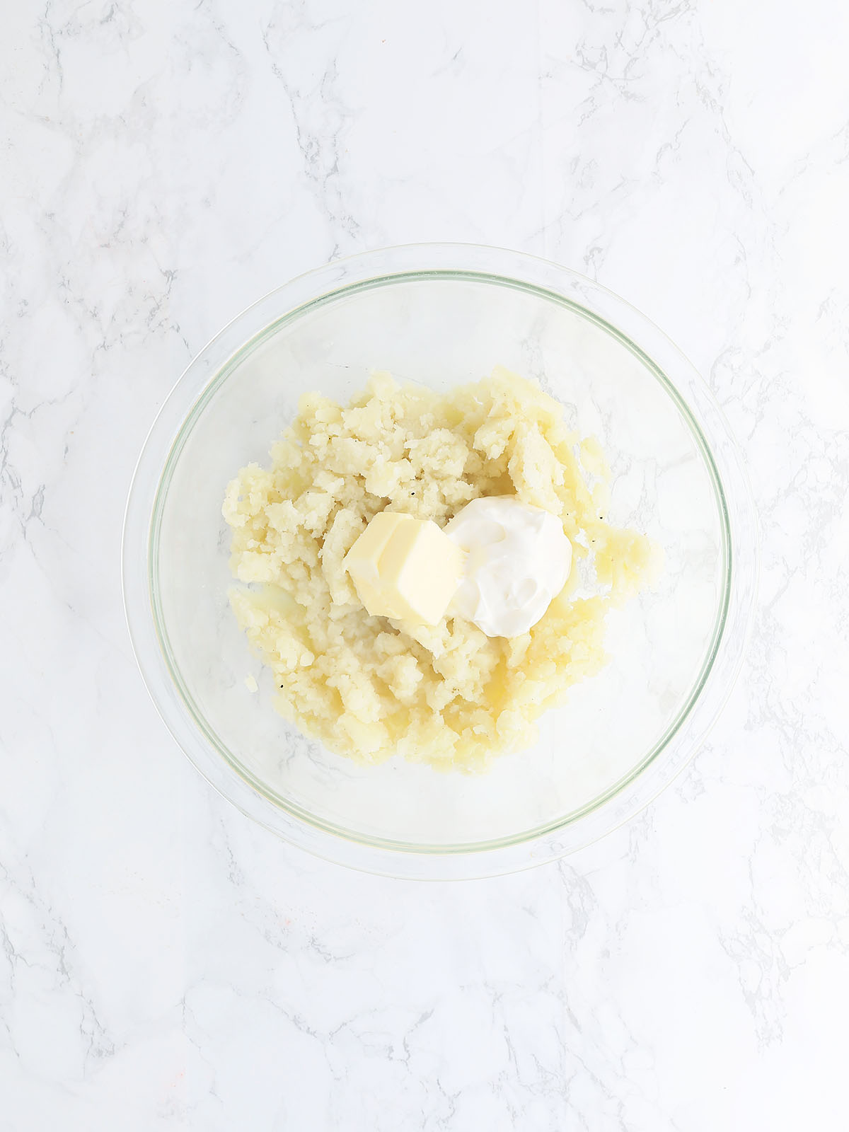 mashed potatoes, softened butter and sour cream in a glass mixing bowl