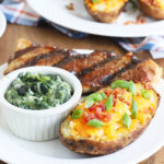twice baked potato on a white plate with a grilled steak and ramekin of creamed spinach