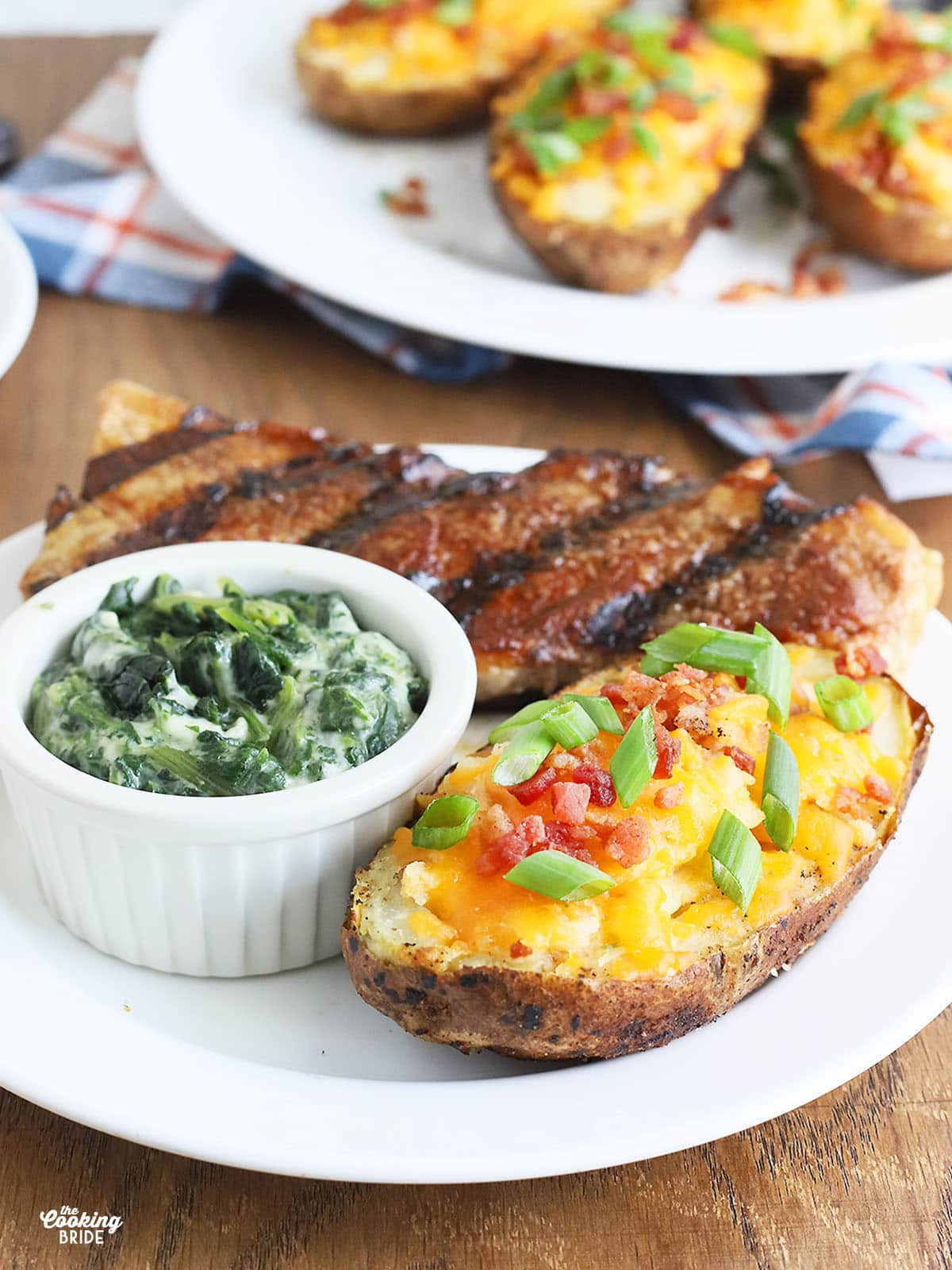 twice baked potato on a white plate with a grilled steak and ramekin of creamed spinach
