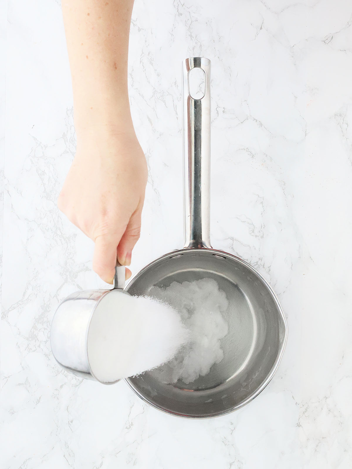 pouring sugar into the water in a stainless steel saucepan