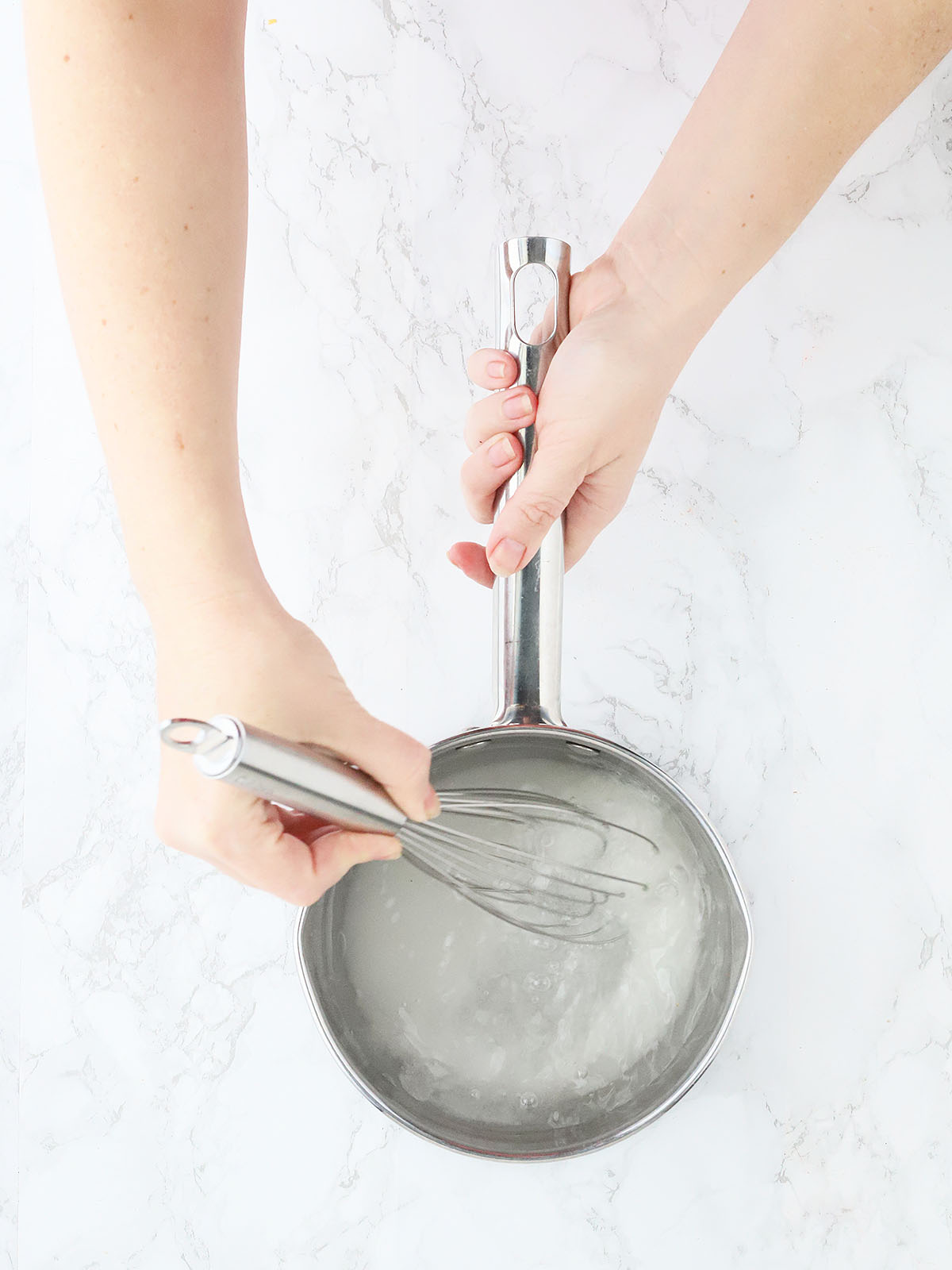 hand whisking sugar and water together in a stainless steel saucepan