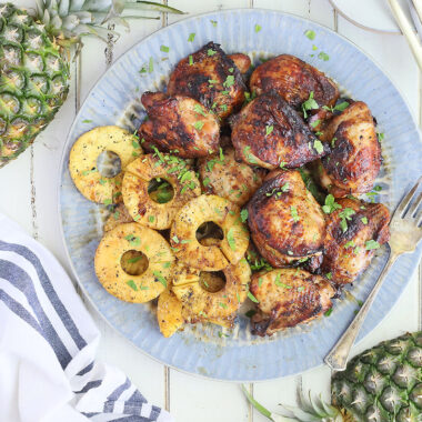 grilled pineapple chicken thighs and grilled pineapple rings on a blue platter with halved pineapple on the side