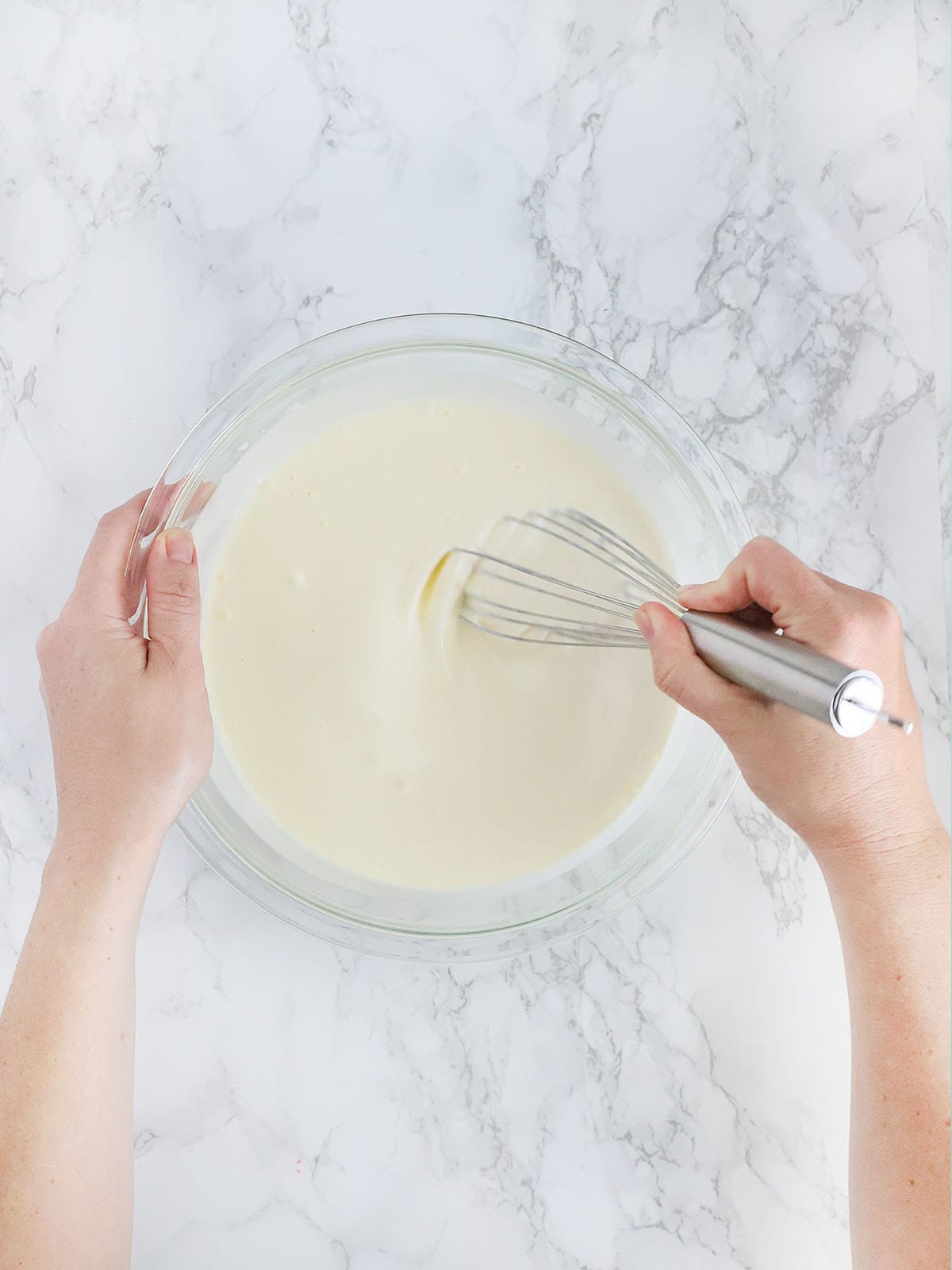hands whisking together mayonnaise and buttermilk in a glass bowl