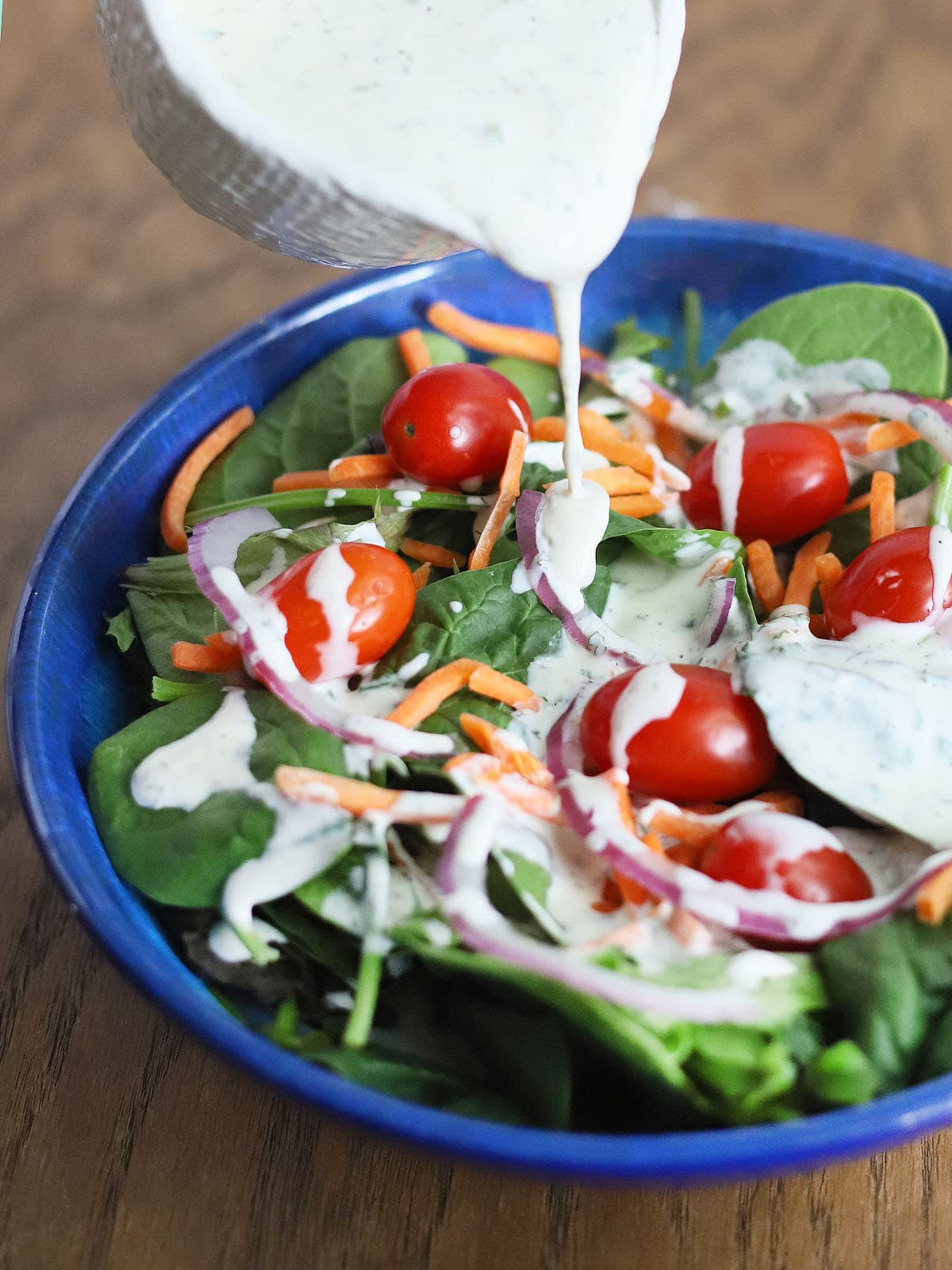 pouring buttermilk ranch dressing over a salad in a blue bowl