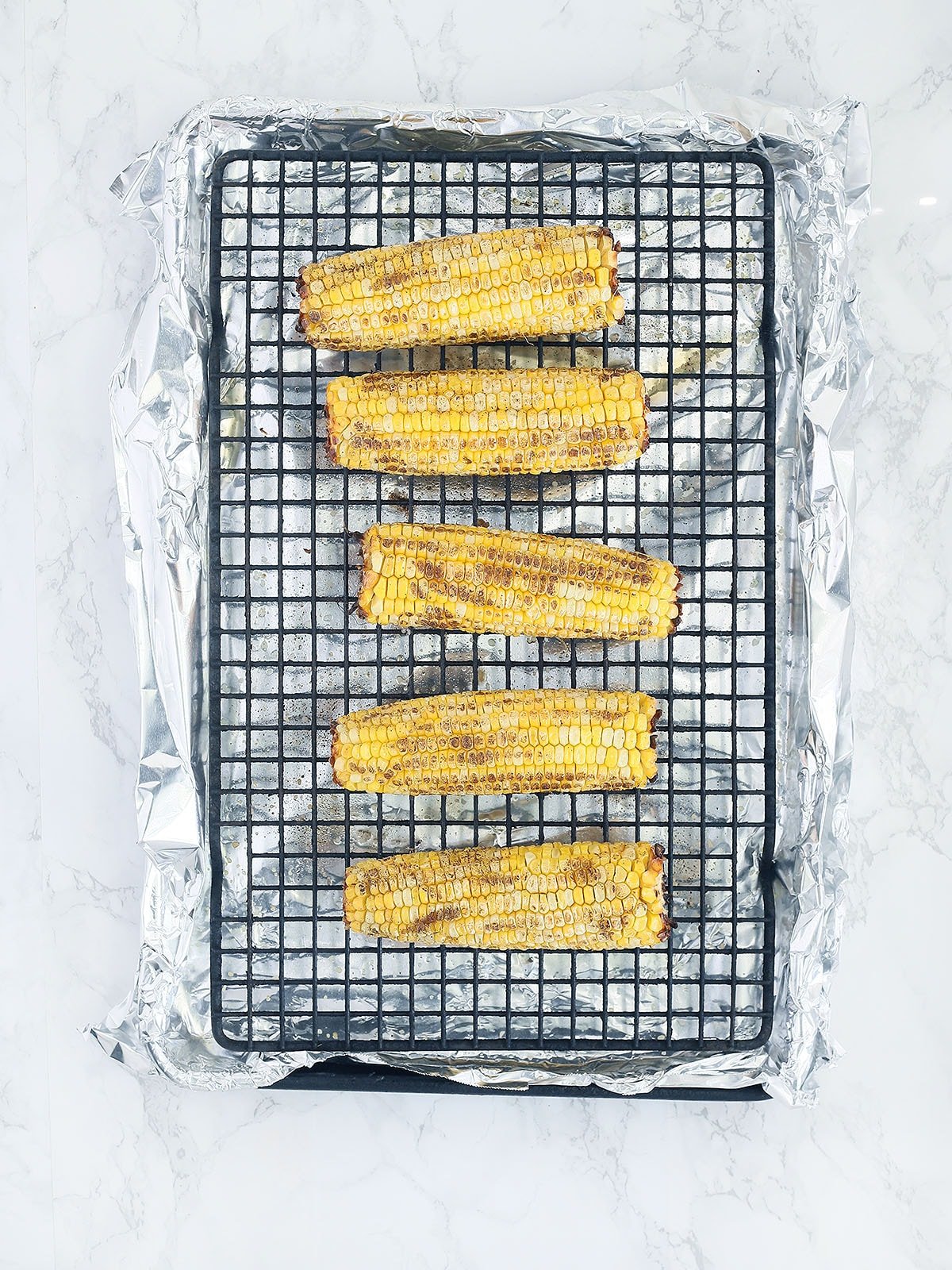 five ears of roasted corn on a baking rack