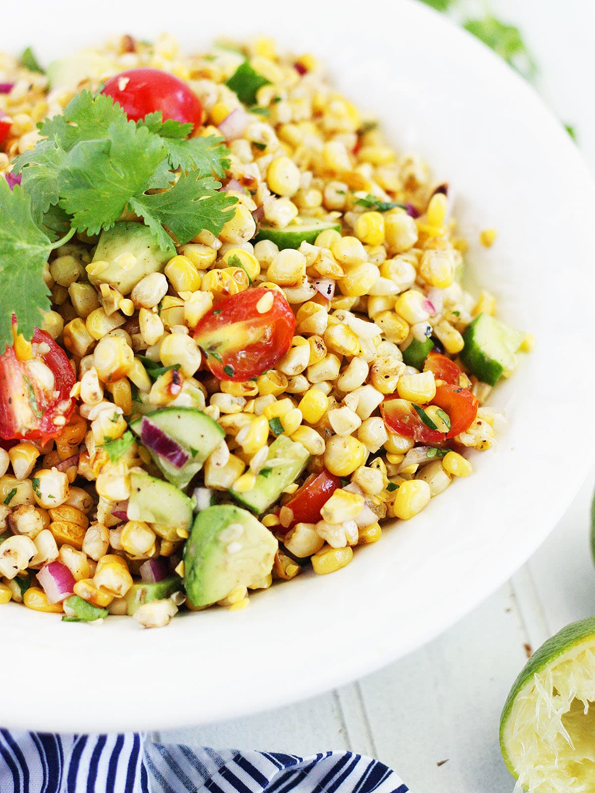 close up of roasted corn salad in a white serving bowl garnished with a sprig of cilantro