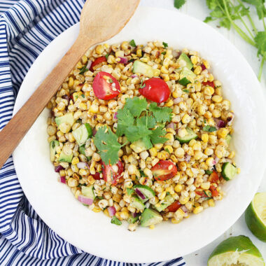 roasted corn salad in a white serving bowl garnished with a sprig of cilantro