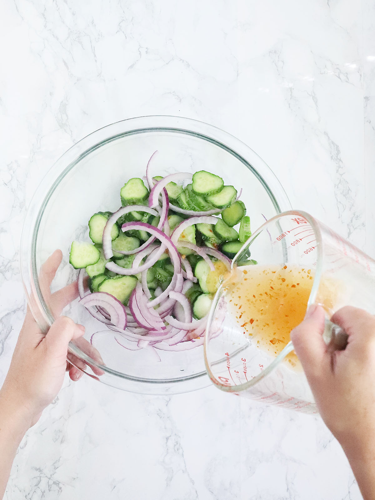 pouring the dressing over the sliced cucumbers and red onions