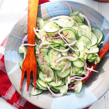 wooden salad tongs in a blue clay bowl with the Asian cucumber salad