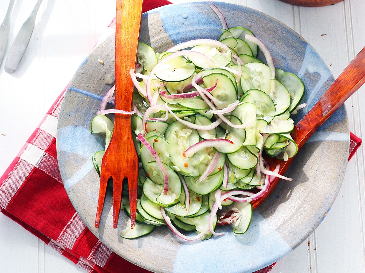 wooden salad tongs in a blue clay bowl with the Asian cucumber salad
