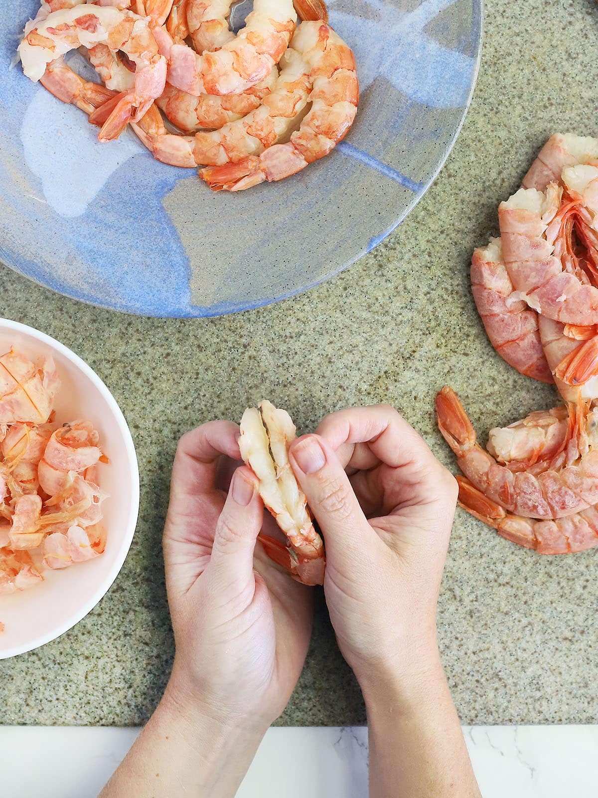 hands pulling back two cut sides of a shrimp to reveal the sand vein