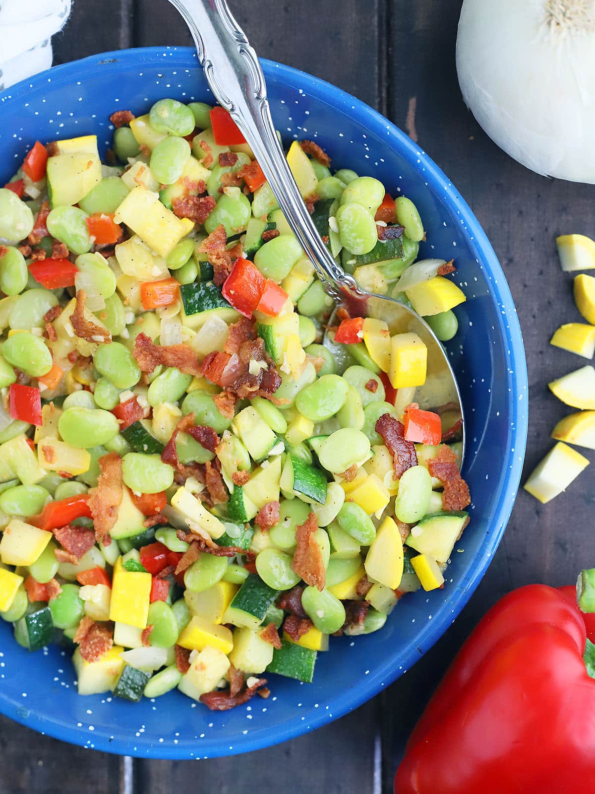 summer succotash in a blue enamel skillet with an onion, red bell pepper and diced squash to the side