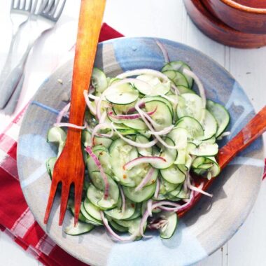 wooden salad tongs in a blue clay bowl with the Asian cucumber salad