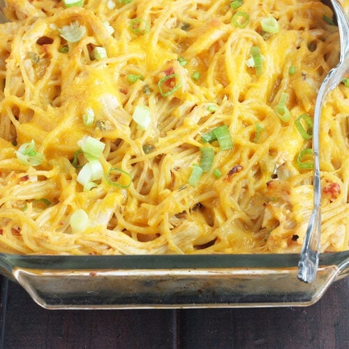 clear pyrex dish of baked chicken spaghetti with a metal serving spoon