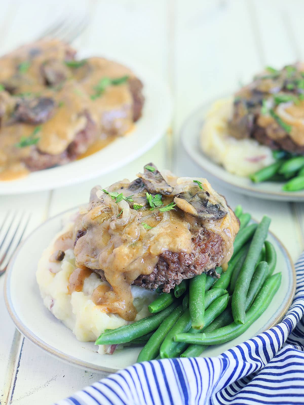 hamburger steak served over mashed potatoes and green beans covered in mushroom gravy