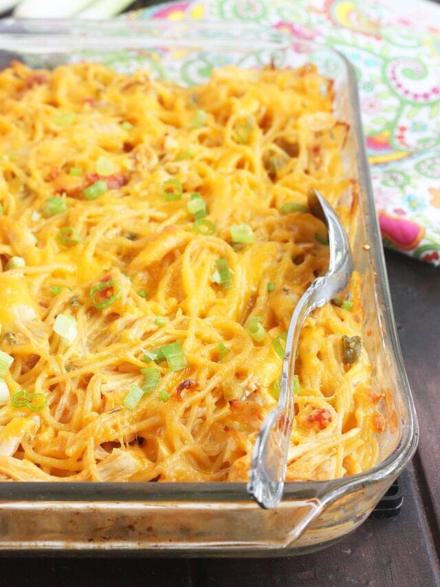 clear pyrex dish of baked chicken spaghetti with a metal serving spoon