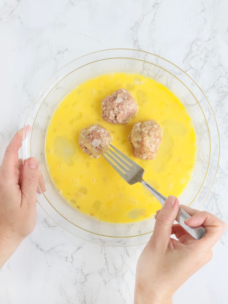hands coating three meatballs with egg