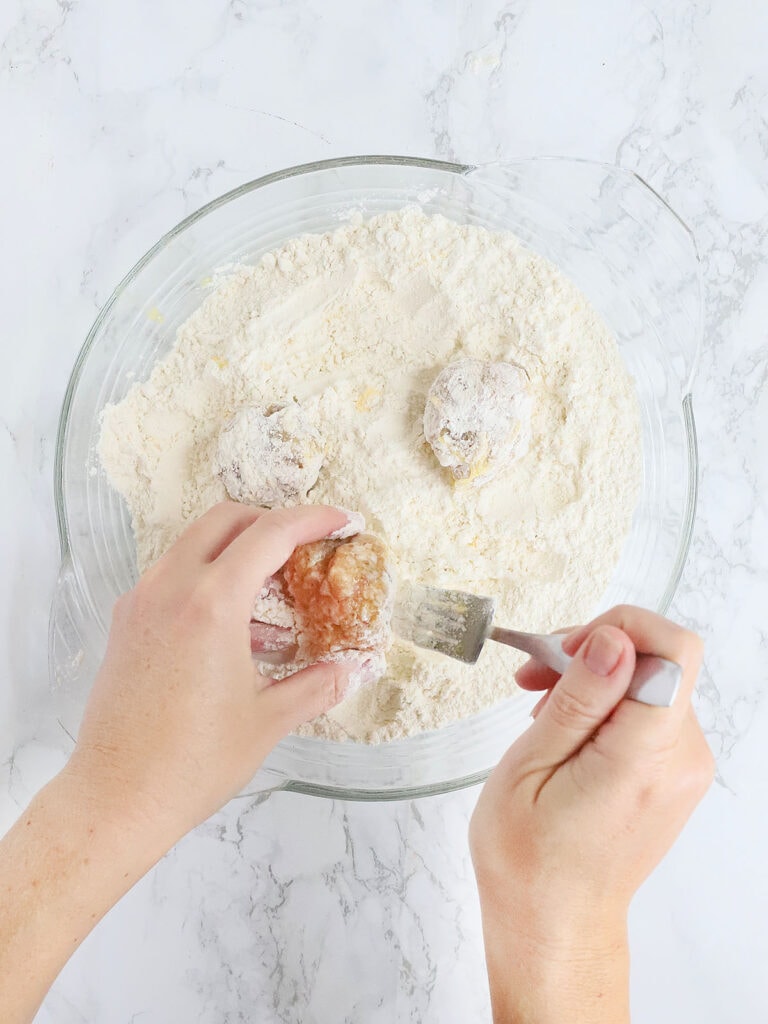 hands coating the chicken meatballs in flour